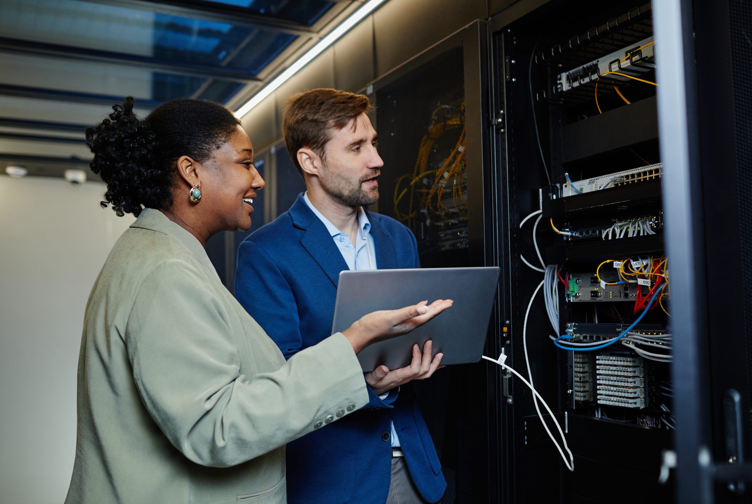 In a bustling data center, two professionals meticulously examine server equipment, with one expertly holding a laptop. Their focus is unwavering as they assess the intricate systems, ensuring seamless operations through their expertise in managed IT services.