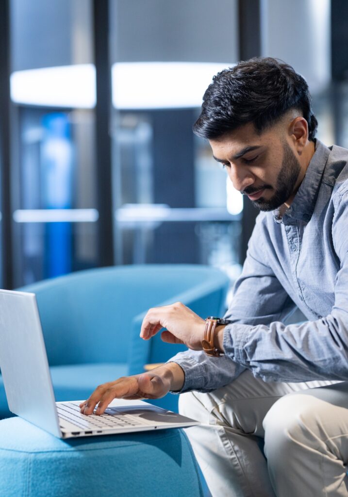 Using laptop, man checking time on smartwatch while working in modern office, copy space