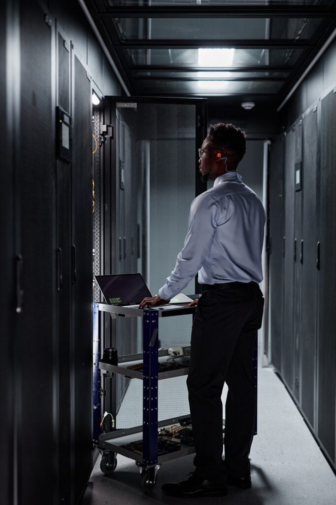 Full length network engineer using laptop and setting up servers in data center