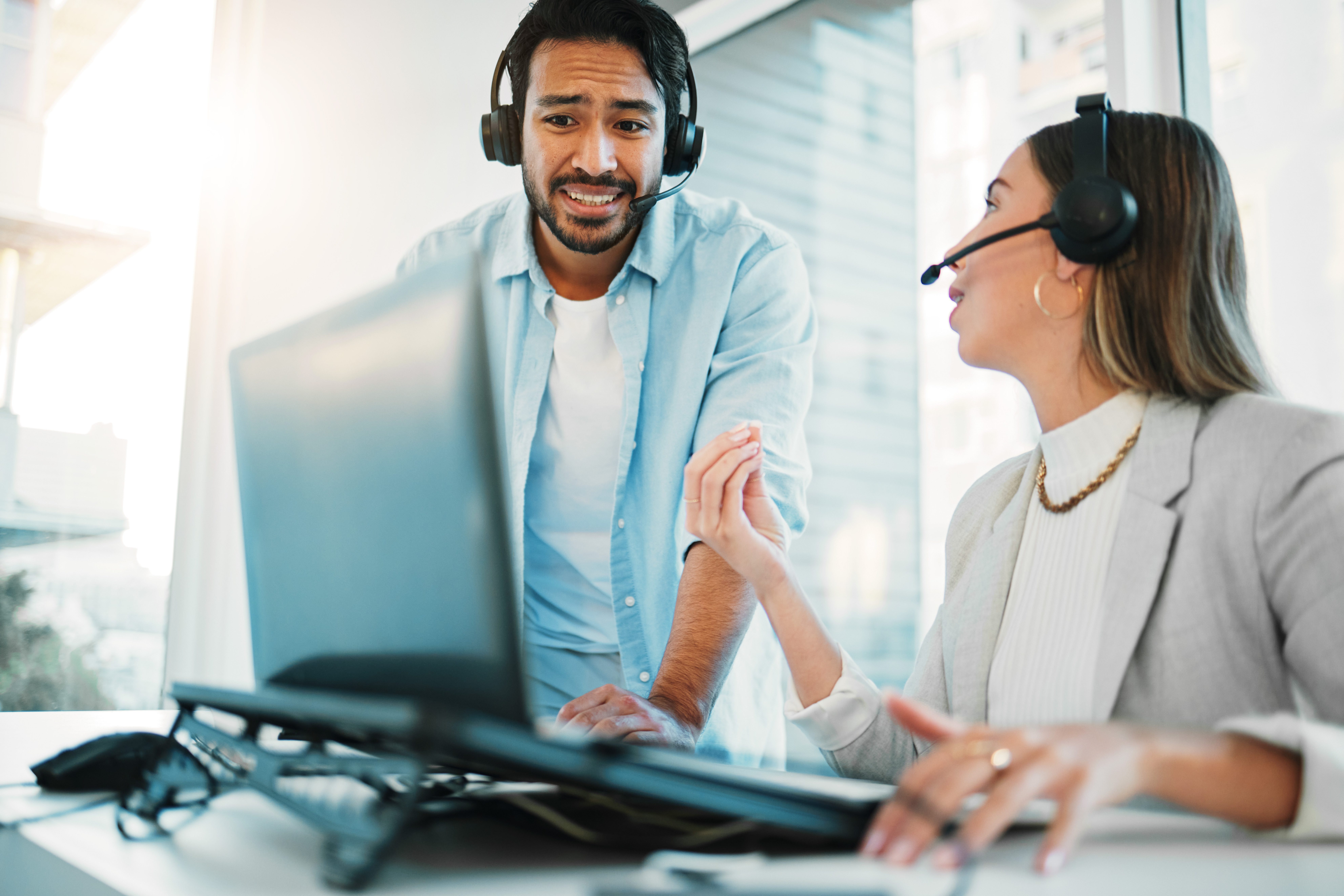 Two people wearing headsets are having a discussion about cloud management while looking at a laptop in an office setting.