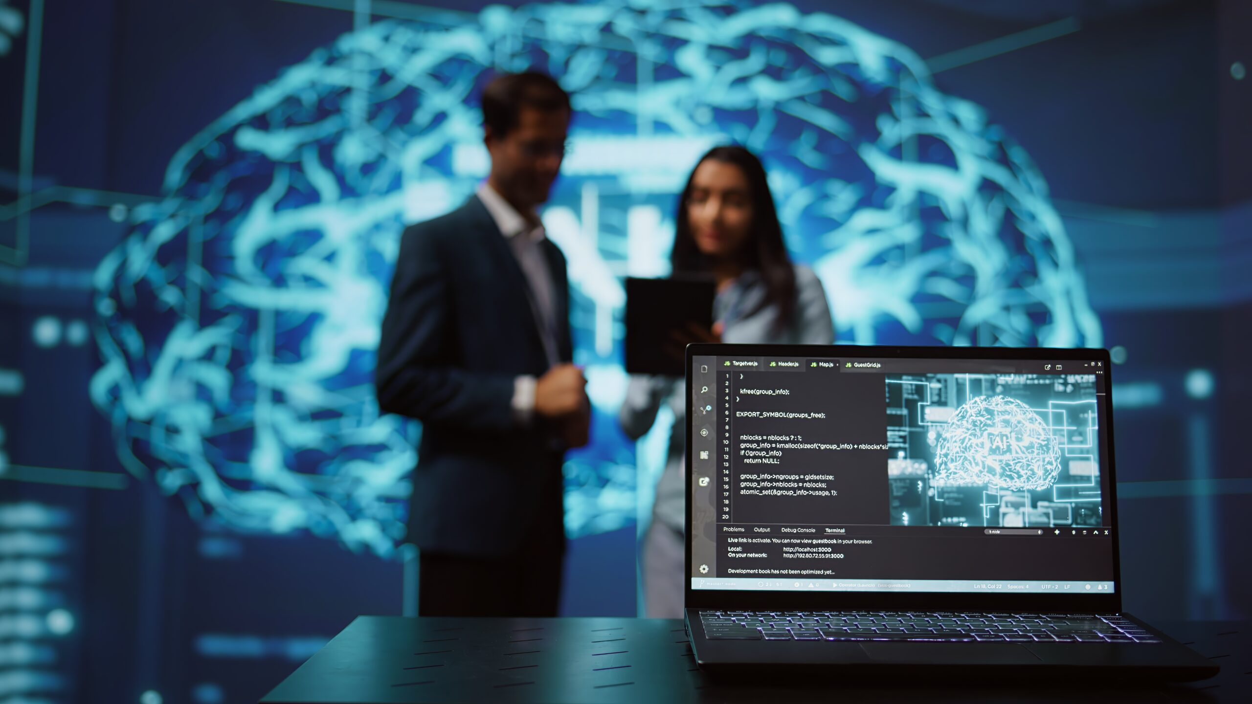 A laptop displays code and a digital brain image, showcasing AI solutions, while two people in the background discuss something with a large brain illustration on the wall.