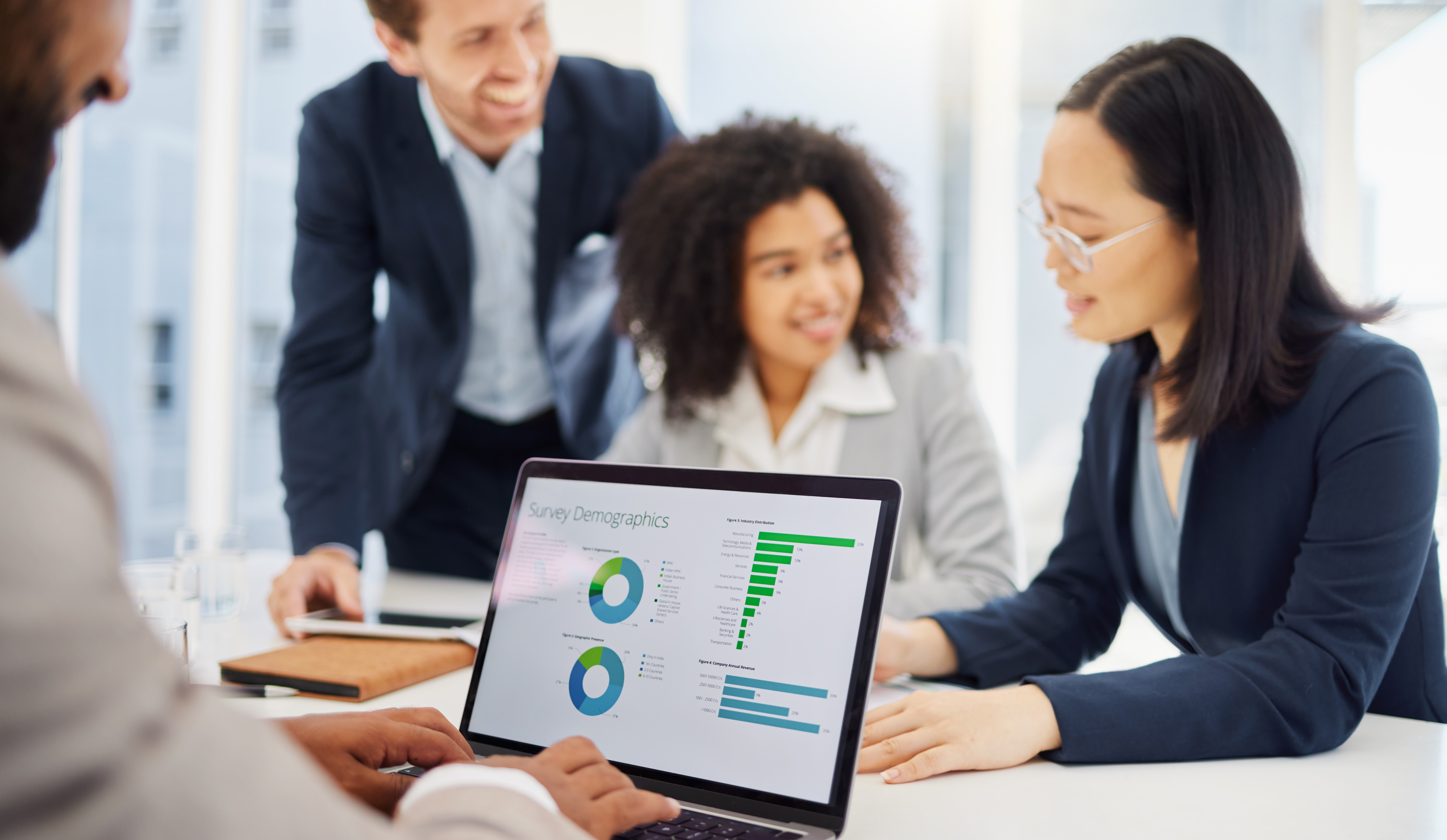 A group of professionals is immersed in discussing charts on a laptop, utilizing a virtual desktop in their bright office setting.