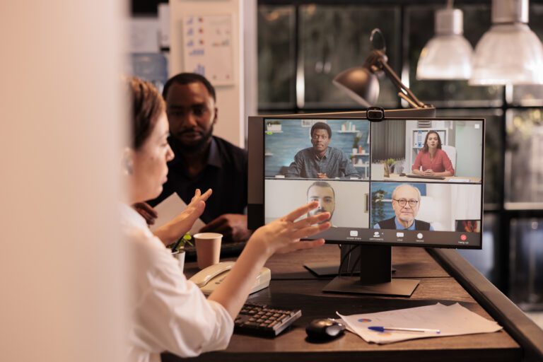 A group of people in an office participates in a video conference call, seamlessly using their virtual desktop, with four colleagues visible on the computer screen.