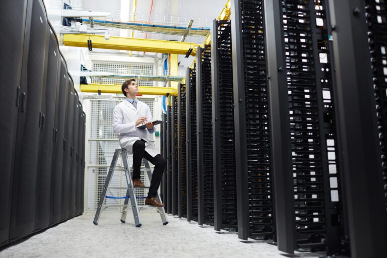 A person in a lab coat stands on a stepladder, meticulously inspecting server racks in a cloud data center, tablet in hand to optimize operations.