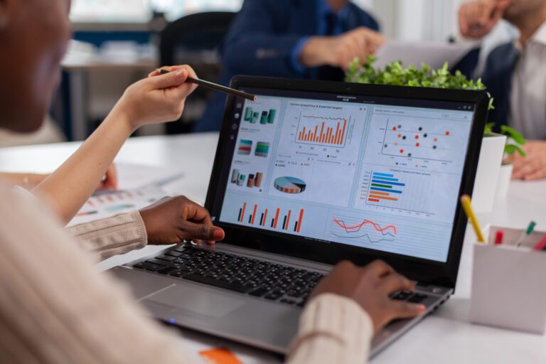 A person points at intelligent analytics visualizations on a laptop screen in an office setting.