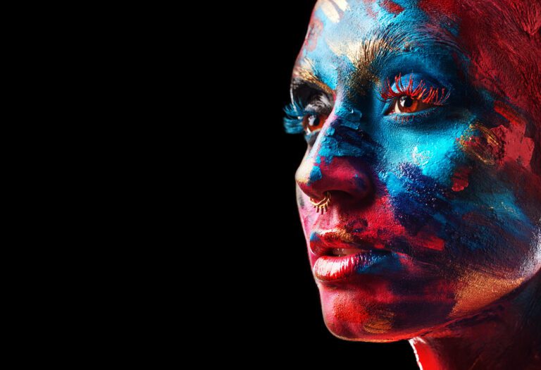 Close-up of a person with an elaborate red, blue, and yellow design painted on their face, resembling a work created through generative AI, set against a black background.