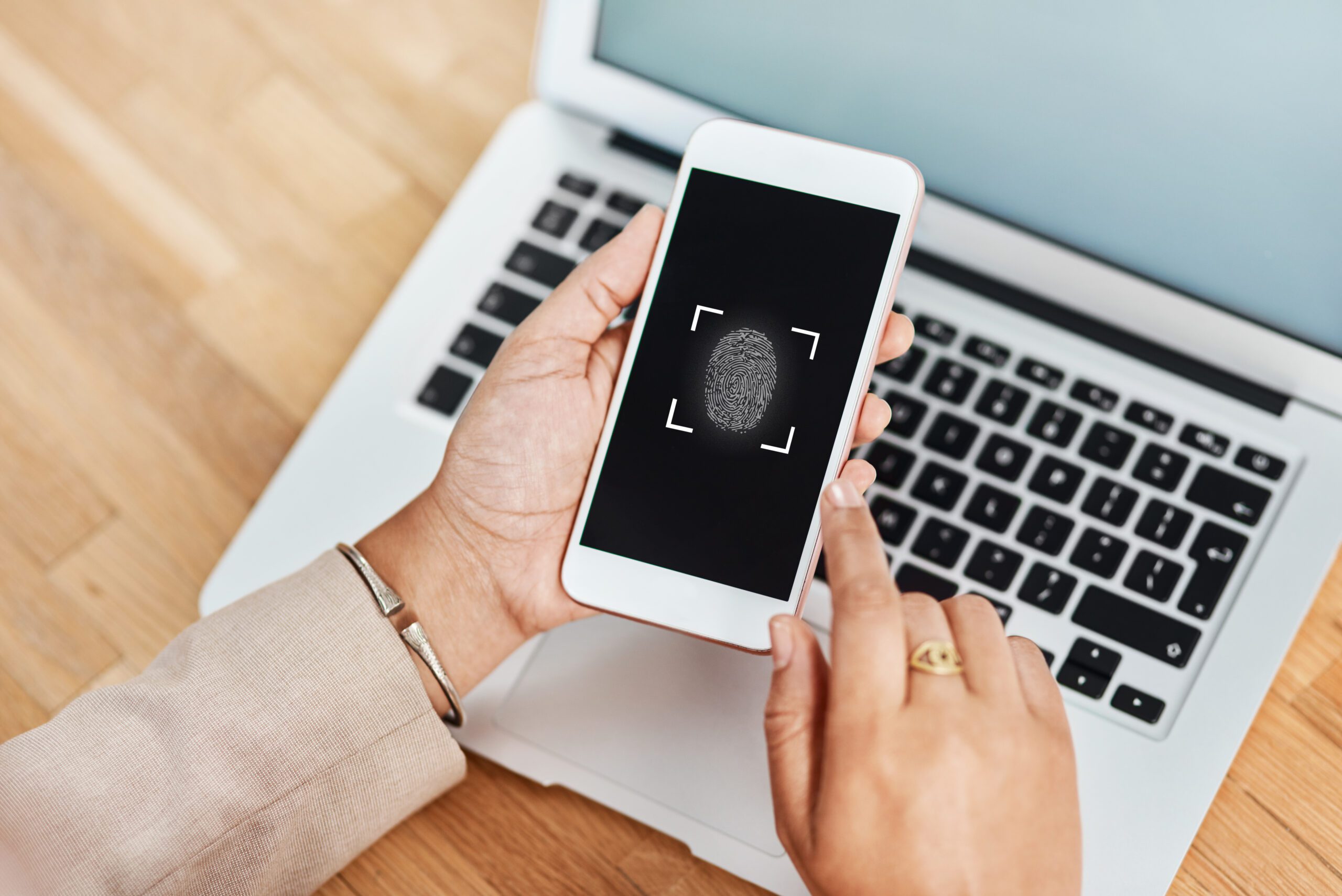 A person holds a smartphone displaying a fingerprint scanner, seamlessly ensuring secure connectivity as it hovers above a laptop on a wooden surface.