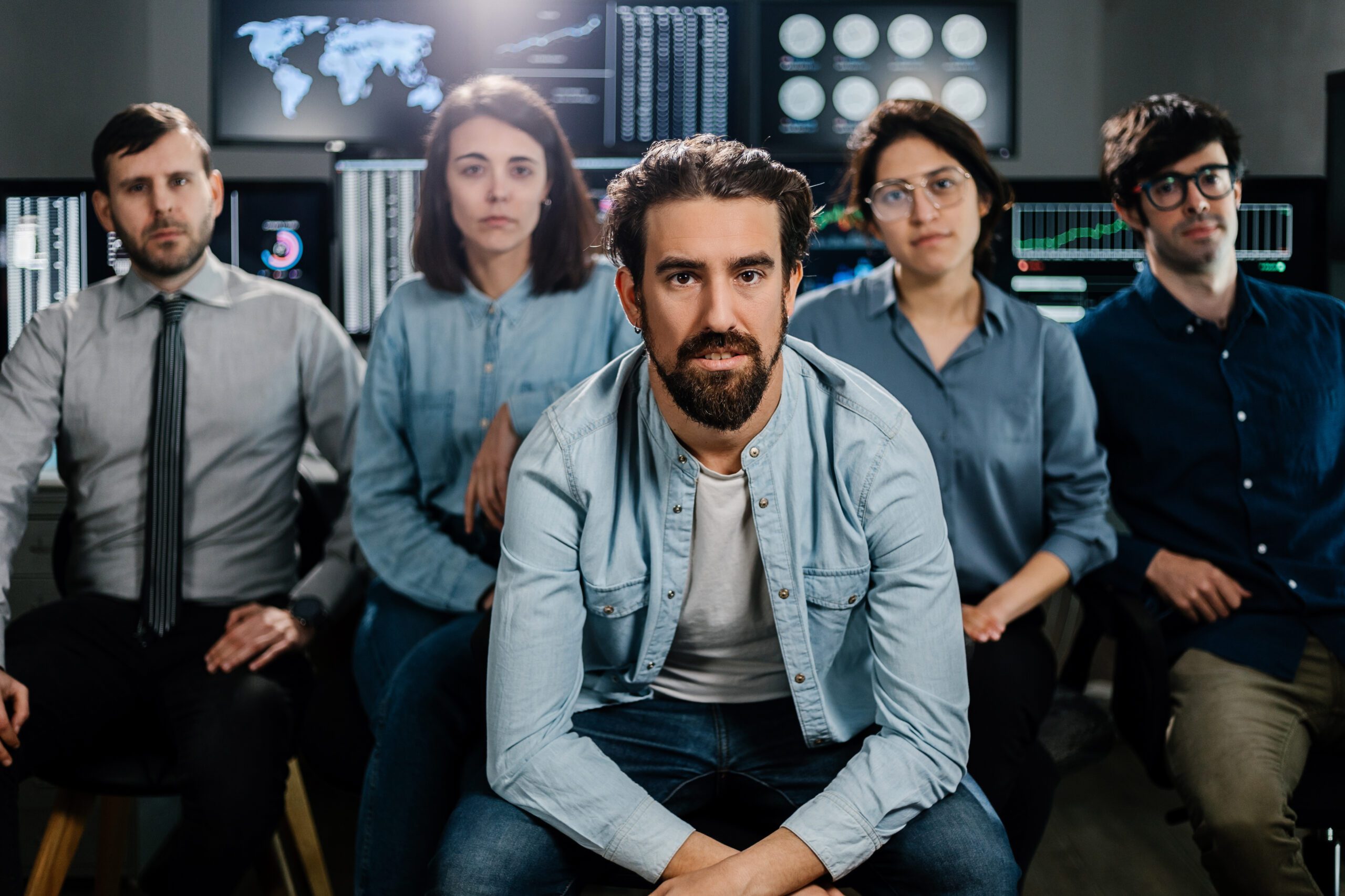 A group of five people in casual attire sit and pose in a room with multiple computer screens displaying data, focusing on threat detection and response.