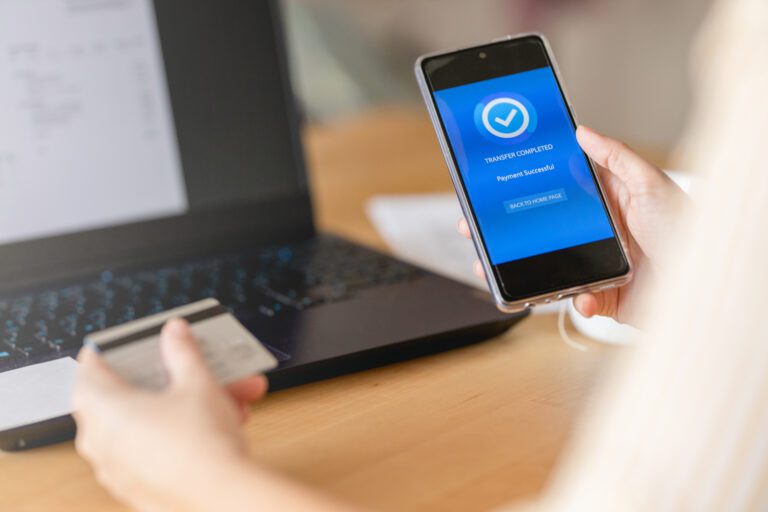 Person holding a smartphone with a "Payment Successful" screen next to a laptop, assuring secure connectivity, while holding a credit card.