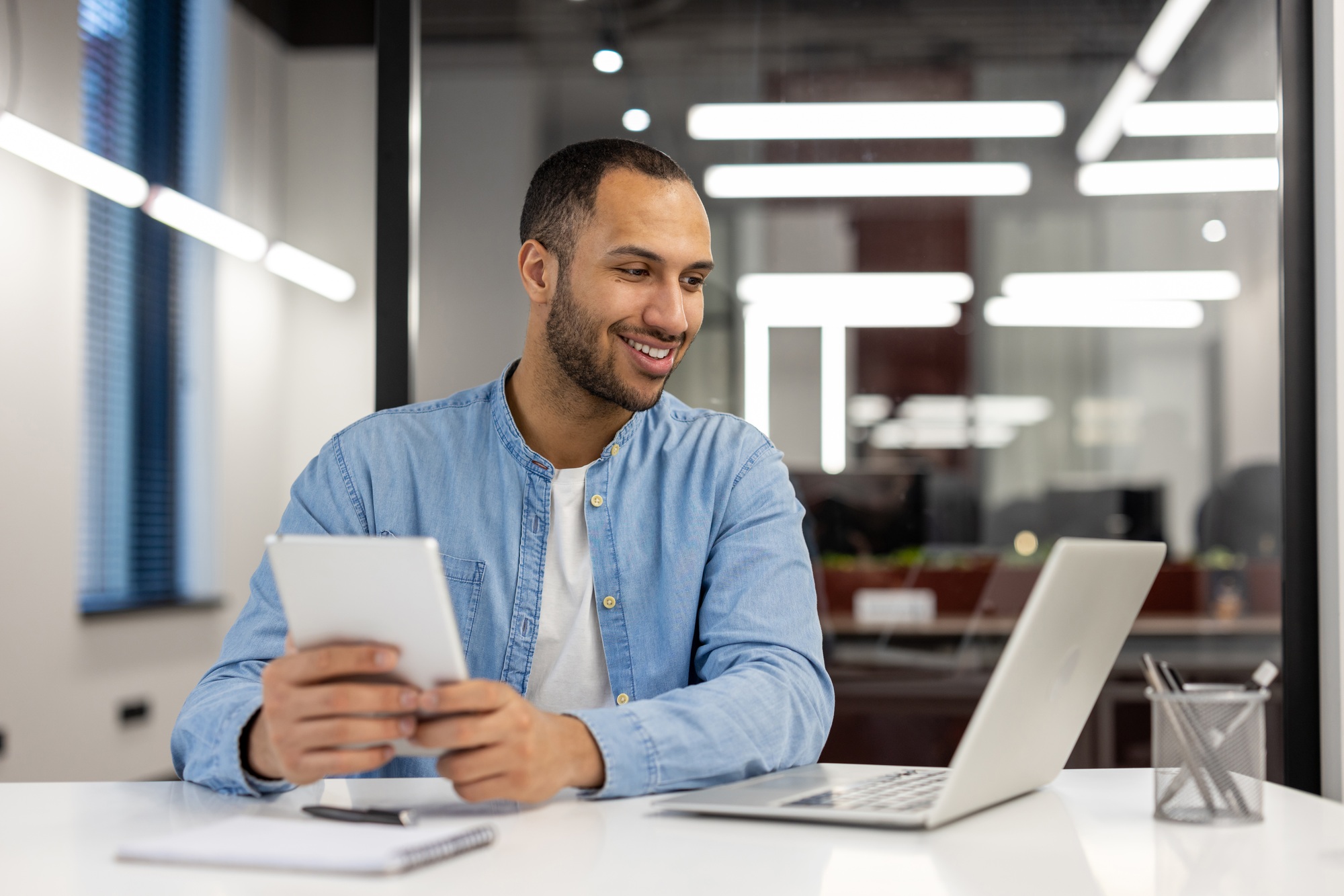 A young Hispanic man is talking on a video call on a laptop, sitting at a desk in the office