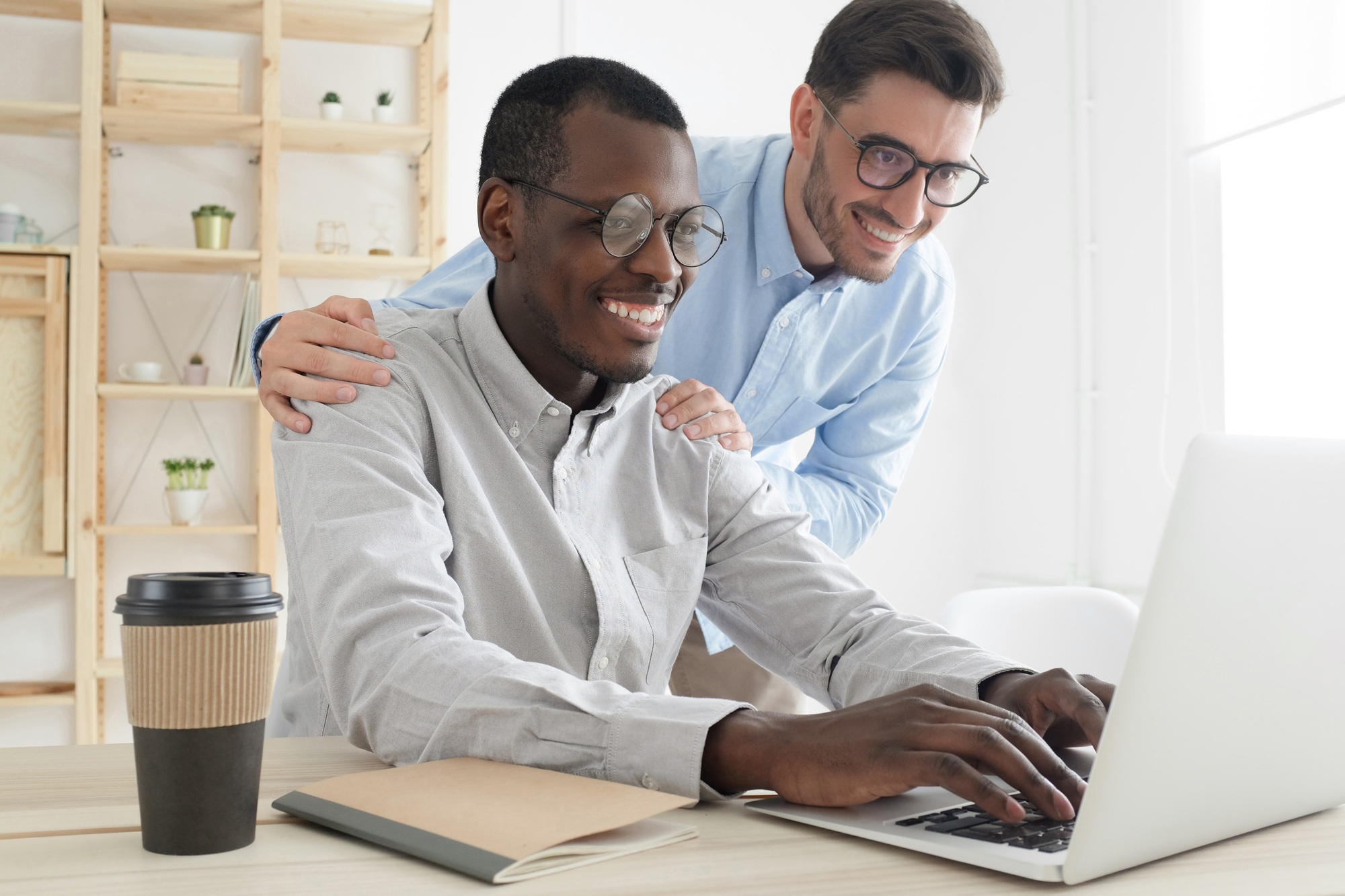 Friendly boss suppoting and explaining new task to smiling young employee, looking at laptop screen