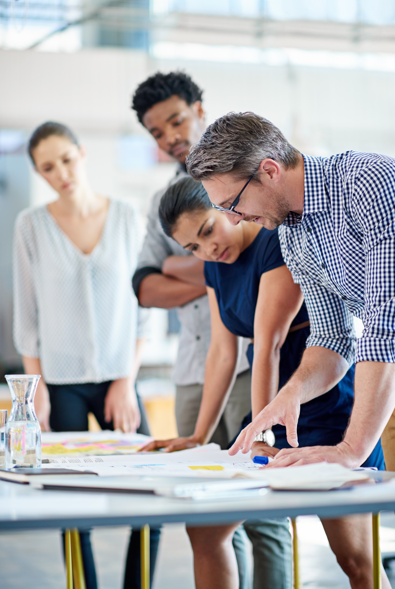 Male and female managers planning at a table with younger staff members looking on