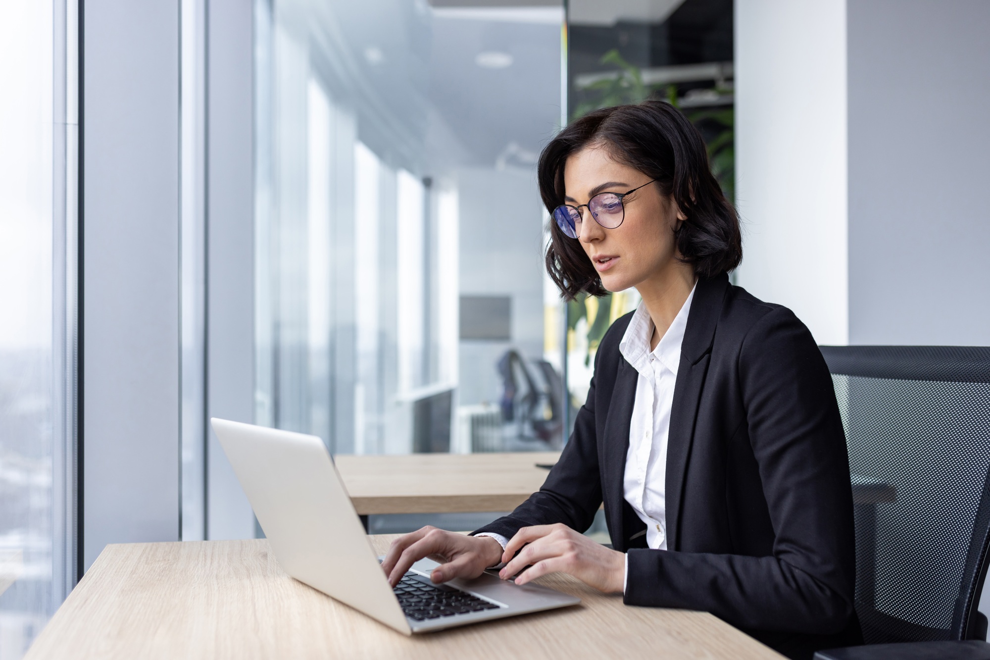 Serious confident thinking businesswoman at work with laptop inside office, female office worker in