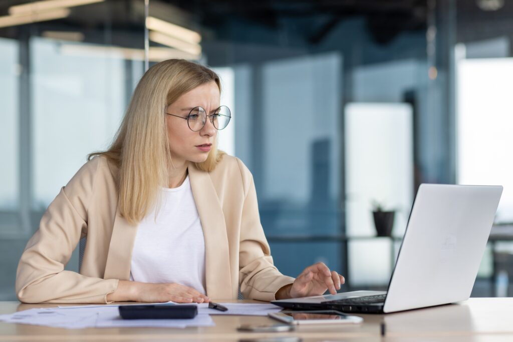 Worried and focused businesswoman working in the office on a laptop and with documents. Type on the