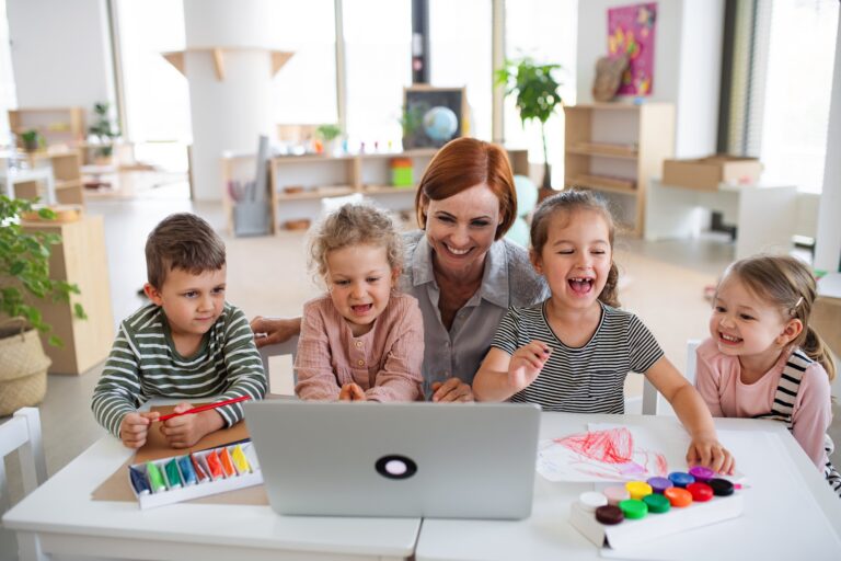 Group of small nursery school children with teacher indoors in classroom, using laptop