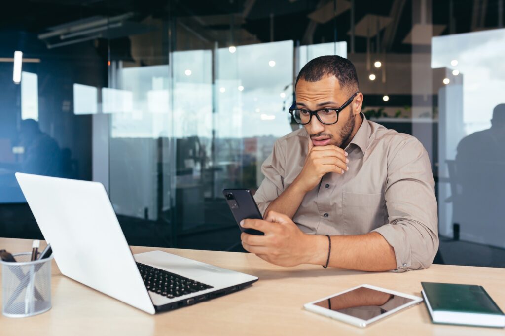 Thinking african american businessman reading news on smartphone, man working inside office at work