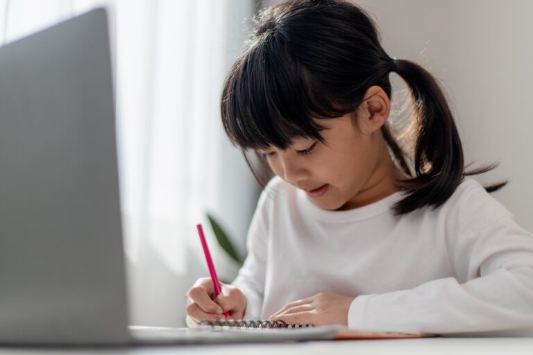 Asian schoolgirl doing her homework with laptop at home. Children use gadgets to study.