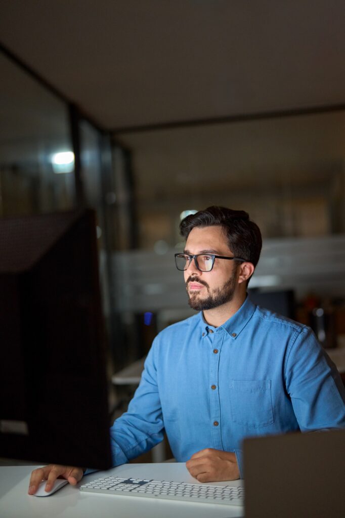 Busy young business man using computer working late in office. Vertical.