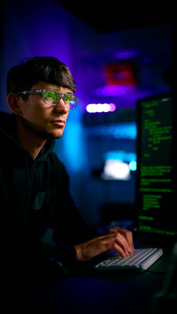 Low Key Lighting Shot Of Male Computer Hacker Sitting In Front Of Screens Breaching Cyber Security