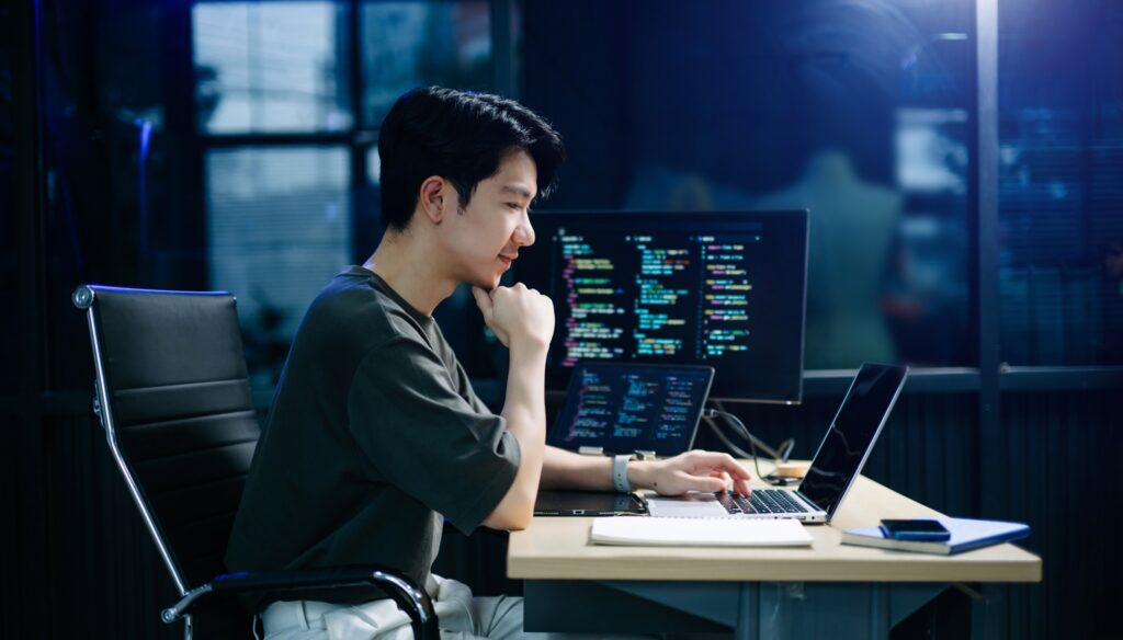 Asian developer writing code at night in modern office setup. Concept of software engineering,