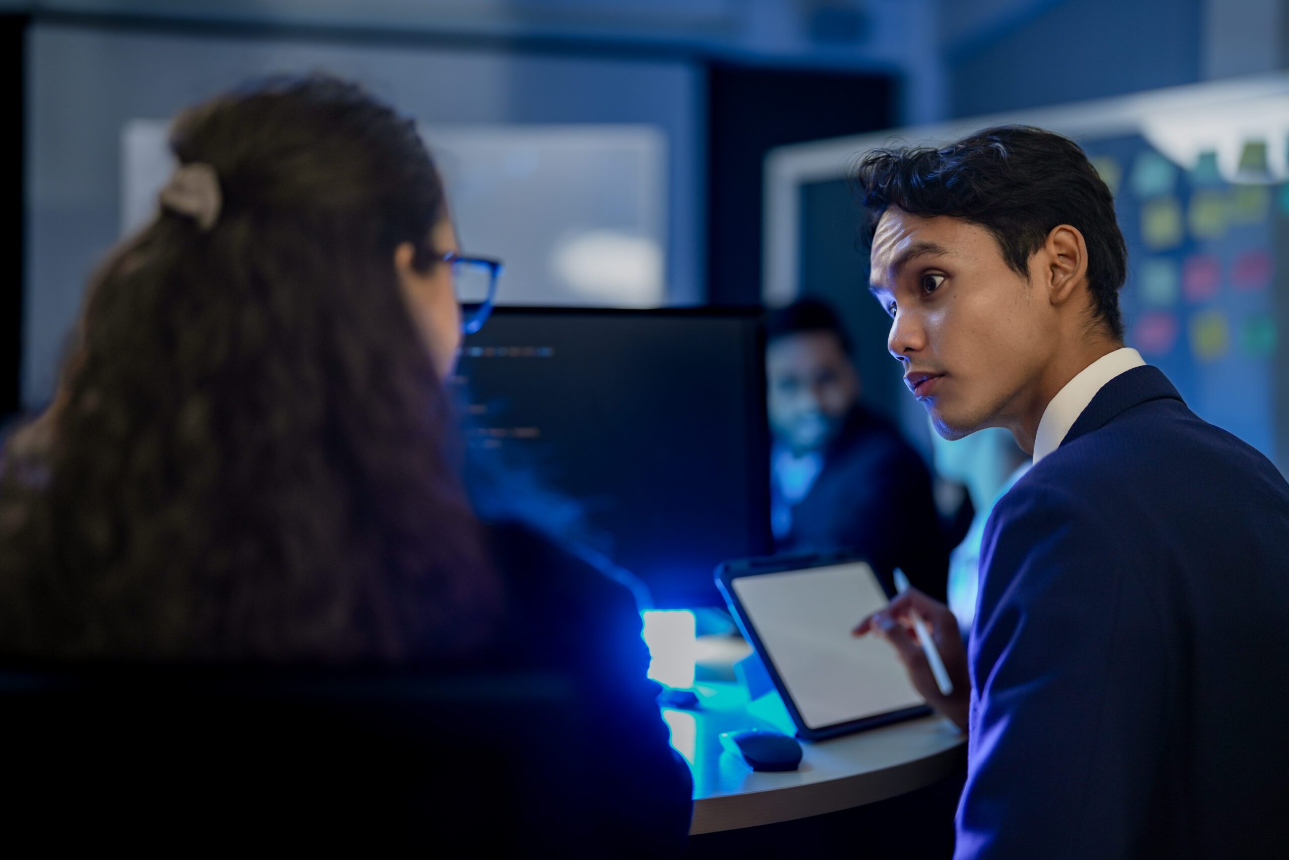 A diverse team of AI developers collaborates on a night coding session. A senior engineer oversees his team, intensely focused on debugging a complex machine learning project.