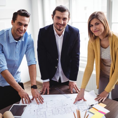 Portrait of smiling business people with blueprint at creative office
