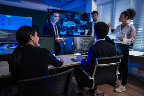Strategic team meeting in an office command center, reviewing automotive AI development project dashboards under cool blue night lighting.